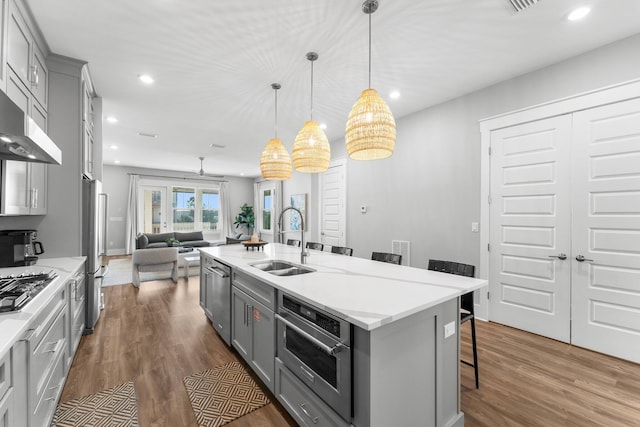 kitchen featuring appliances with stainless steel finishes, sink, gray cabinetry, a kitchen bar, and a kitchen island with sink