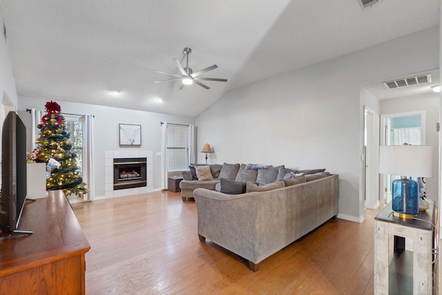 living room with a tiled fireplace, ceiling fan, hardwood / wood-style floors, and vaulted ceiling