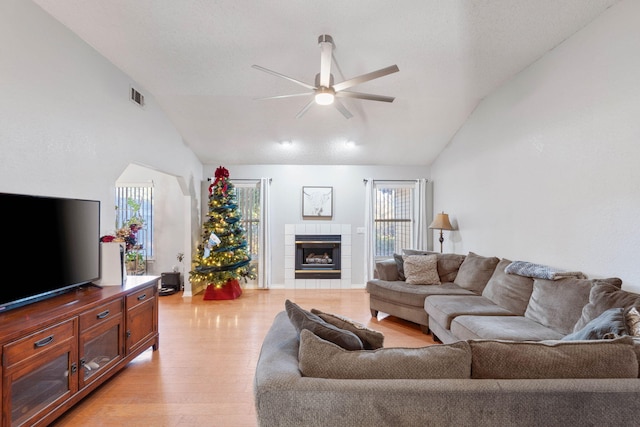 living room featuring a healthy amount of sunlight, light wood-type flooring, lofted ceiling, and a tile fireplace