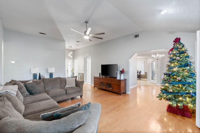 living room featuring ceiling fan with notable chandelier, light hardwood / wood-style flooring, a textured ceiling, and vaulted ceiling