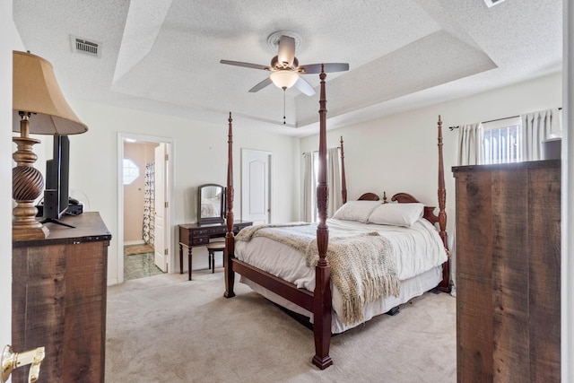 bedroom featuring ensuite bathroom, a raised ceiling, ceiling fan, a textured ceiling, and light colored carpet