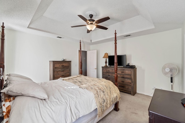 bedroom featuring a raised ceiling, ceiling fan, light colored carpet, and a textured ceiling