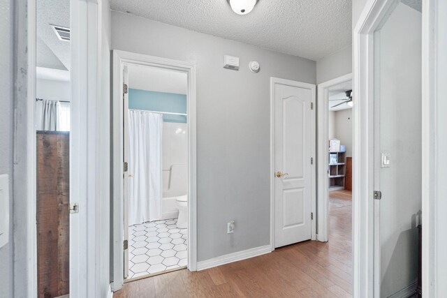 corridor with a textured ceiling and light hardwood / wood-style floors