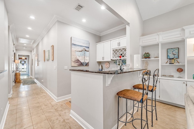 kitchen featuring a breakfast bar, crown molding, dark stone countertops, light tile patterned floors, and white cabinetry