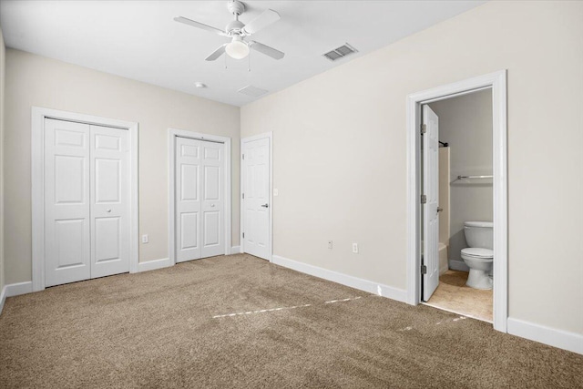 unfurnished bedroom featuring carpet flooring, ceiling fan, connected bathroom, and two closets