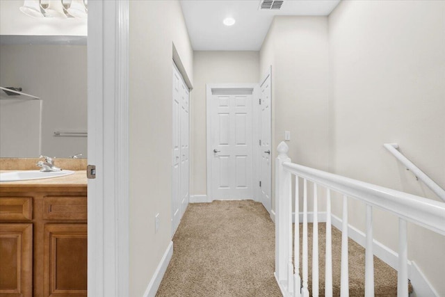 hallway with sink and light colored carpet