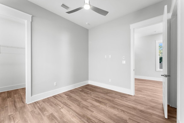 unfurnished bedroom with a closet, a walk in closet, light hardwood / wood-style floors, and ceiling fan