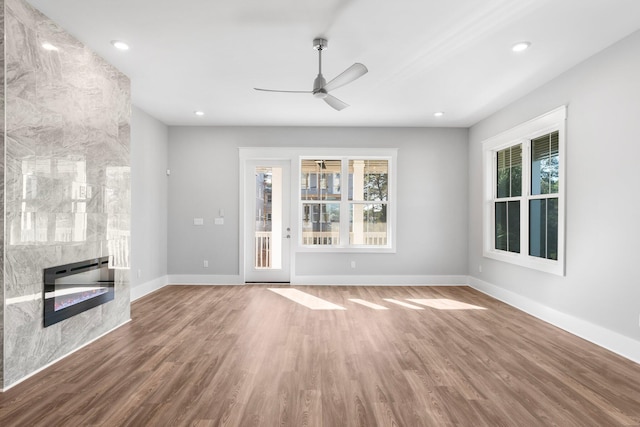 unfurnished living room with hardwood / wood-style floors, ceiling fan, and a tiled fireplace