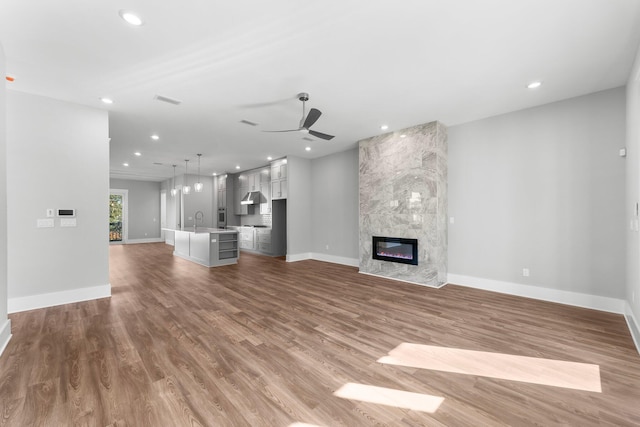 unfurnished living room featuring hardwood / wood-style floors, a large fireplace, ceiling fan, and sink