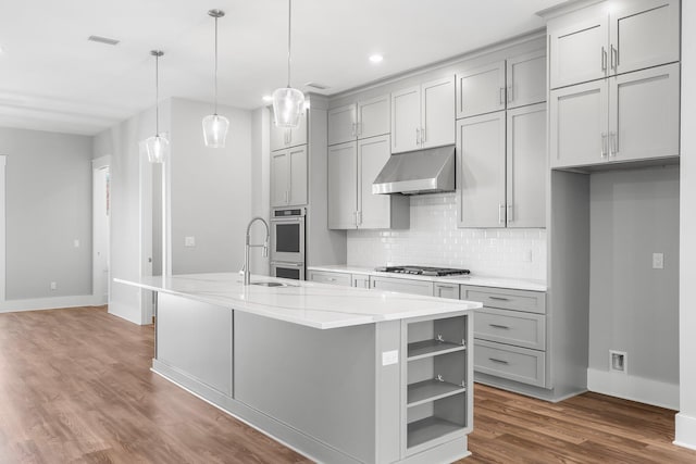 kitchen with light stone countertops, sink, stainless steel appliances, pendant lighting, and a center island with sink