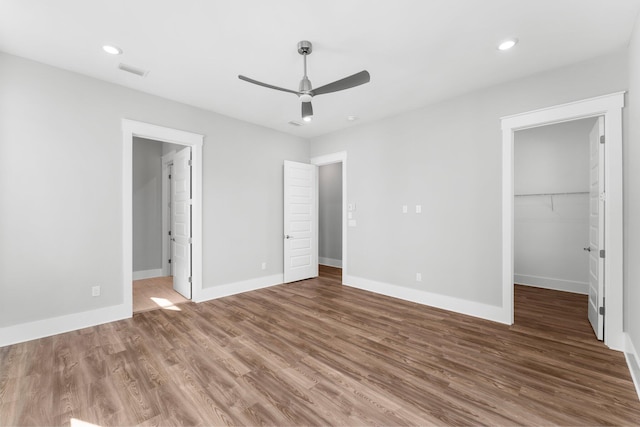 unfurnished bedroom with a walk in closet, ceiling fan, a closet, and hardwood / wood-style flooring