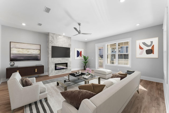 living room with ceiling fan, a large fireplace, and light wood-type flooring