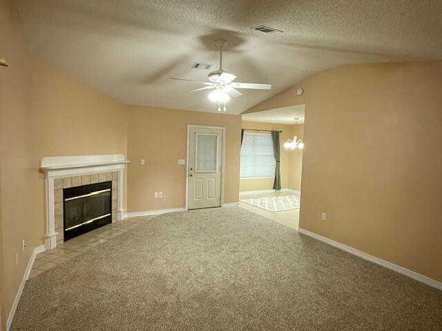 unfurnished living room with light carpet, a textured ceiling, vaulted ceiling, ceiling fan with notable chandelier, and a tile fireplace