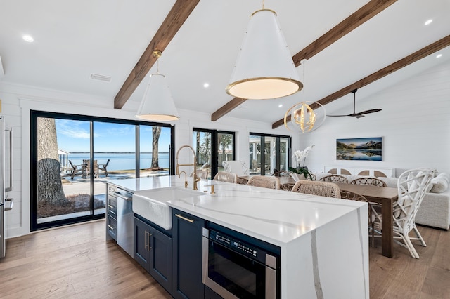 kitchen with appliances with stainless steel finishes, sink, a kitchen island with sink, lofted ceiling with beams, and light hardwood / wood-style flooring