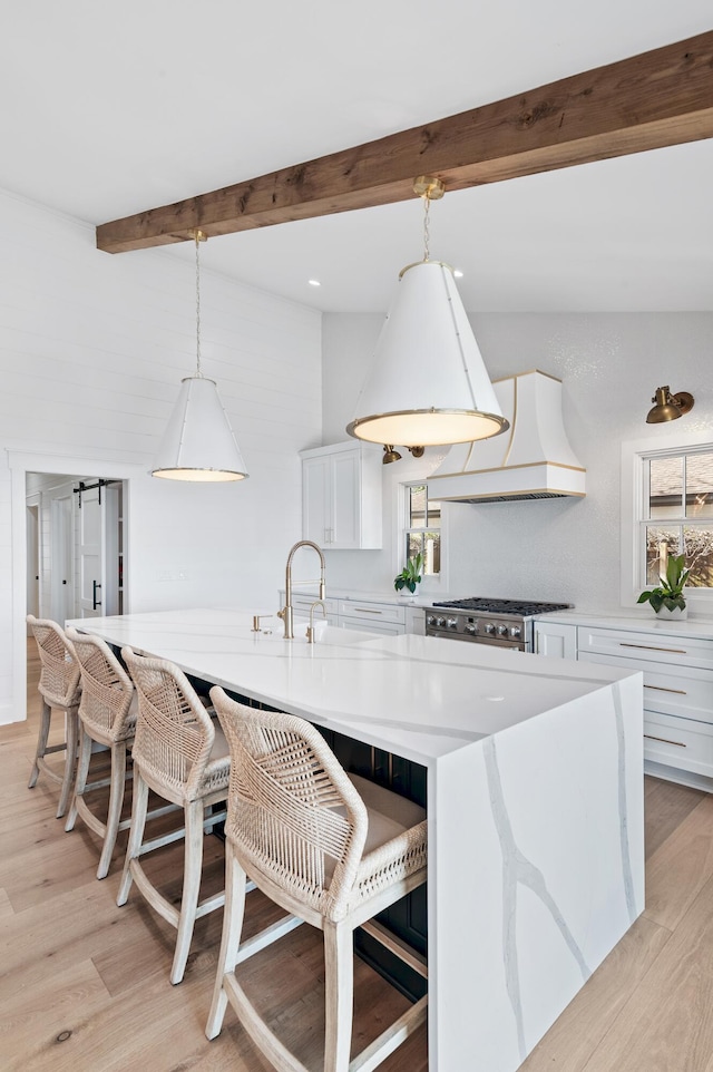 kitchen featuring a center island, white cabinetry, light hardwood / wood-style flooring, hanging light fixtures, and custom range hood