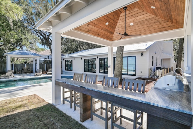 view of patio with ceiling fan, an outdoor kitchen, a gazebo, a fenced in pool, and exterior bar