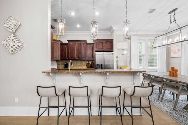 kitchen with stainless steel fridge, a kitchen breakfast bar, tasteful backsplash, crown molding, and hanging light fixtures