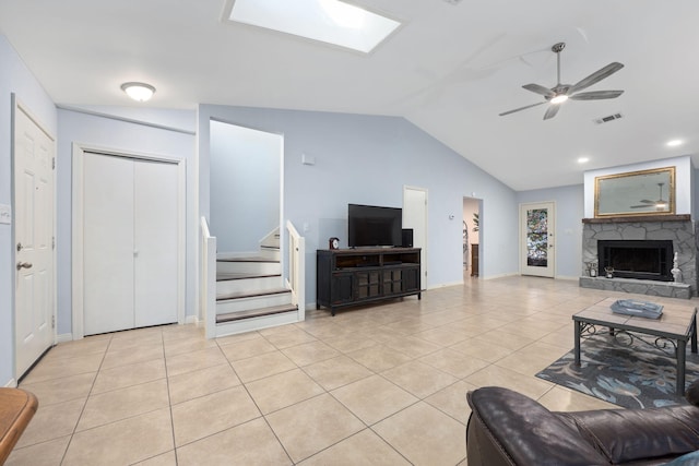 living room featuring ceiling fan, light tile patterned floors, a fireplace, and vaulted ceiling with skylight