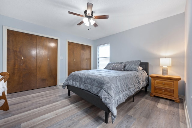 bedroom featuring ceiling fan, two closets, a textured ceiling, and light hardwood / wood-style floors