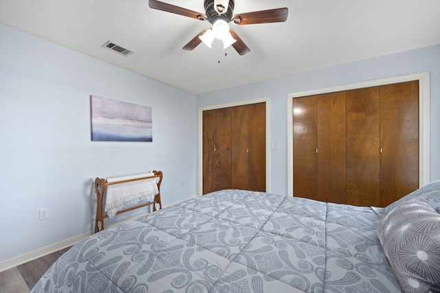 bedroom featuring ceiling fan, a textured ceiling, hardwood / wood-style flooring, and multiple closets