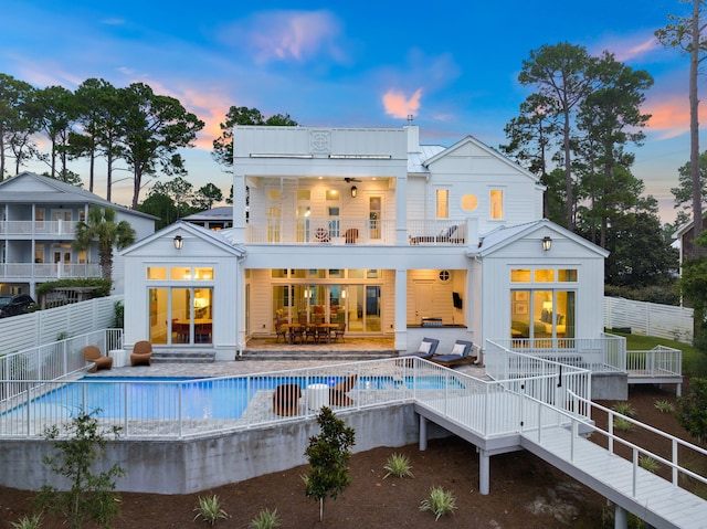 back house at dusk featuring outdoor lounge area, a swimming pool side deck, and a balcony