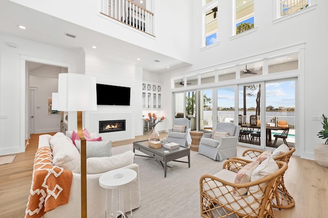 living room featuring ceiling fan, a large fireplace, a towering ceiling, and light hardwood / wood-style flooring