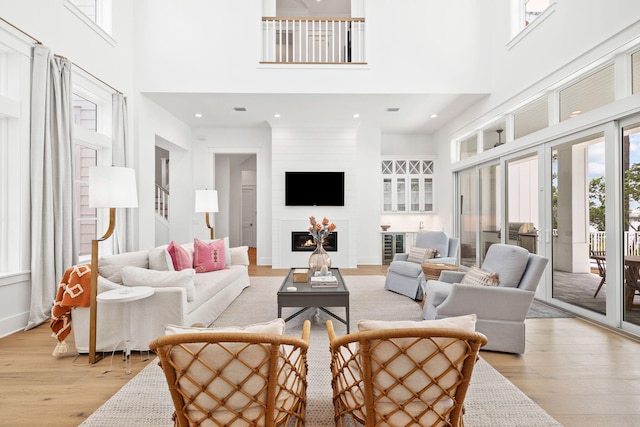 living room featuring a high ceiling, a large fireplace, light hardwood / wood-style flooring, and french doors