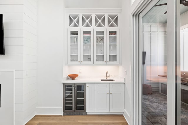 bar featuring white cabinets, light wood-type flooring, beverage cooler, and sink