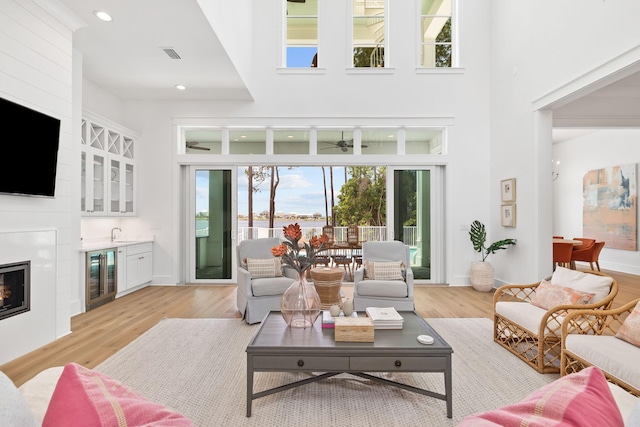 living room featuring light hardwood / wood-style flooring, beverage cooler, a high ceiling, and sink