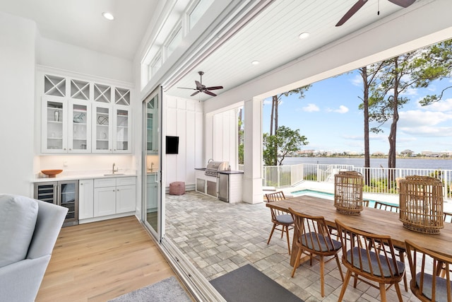 interior space with wine cooler, sink, a water view, and light hardwood / wood-style flooring