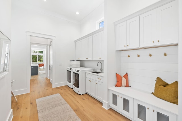 clothes washing area with cabinets, sink, light hardwood / wood-style flooring, washer and dryer, and ornamental molding