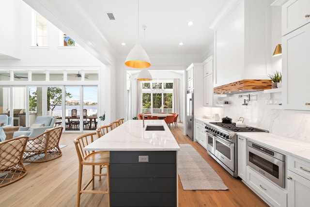 kitchen featuring appliances with stainless steel finishes, backsplash, premium range hood, decorative light fixtures, and white cabinets