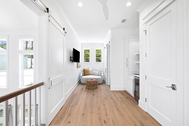 hall featuring a barn door, light hardwood / wood-style flooring, beverage cooler, and ornamental molding