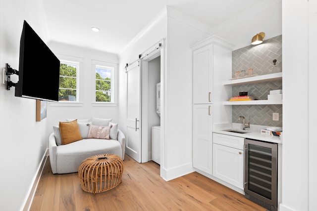 bar featuring sink, beverage cooler, backsplash, stacked washer and dryer, and white cabinets