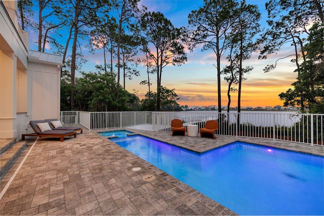 pool at dusk with a patio area and an in ground hot tub