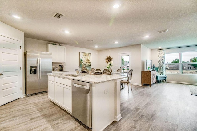 kitchen featuring white cabinetry, light hardwood / wood-style flooring, a textured ceiling, a kitchen island with sink, and appliances with stainless steel finishes