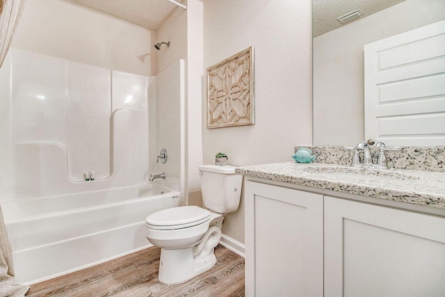 full bathroom with vanity, a textured ceiling, hardwood / wood-style flooring, washtub / shower combination, and toilet