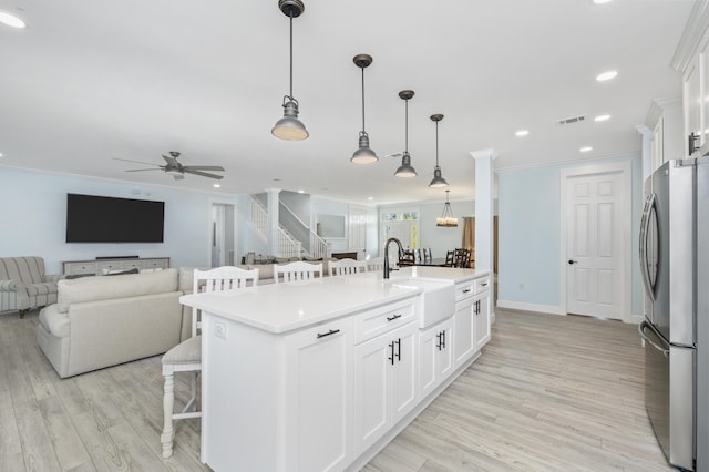 kitchen featuring a breakfast bar, stainless steel refrigerator, white cabinetry, an island with sink, and sink