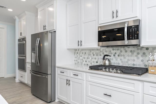 kitchen with appliances with stainless steel finishes, light wood-type flooring, decorative backsplash, and white cabinets