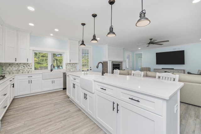 kitchen featuring sink, crown molding, decorative light fixtures, a center island with sink, and white cabinets