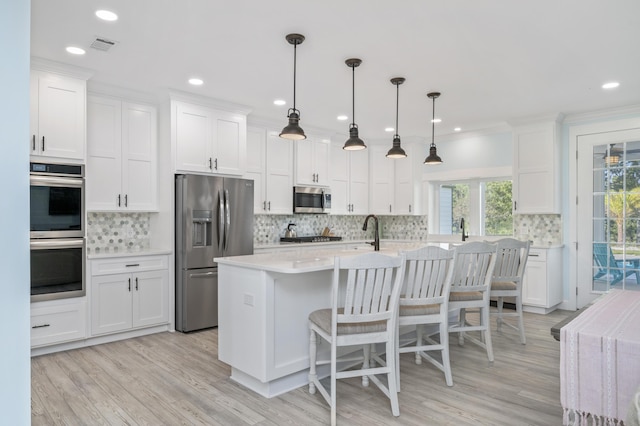 kitchen with a center island with sink, appliances with stainless steel finishes, hanging light fixtures, and white cabinets