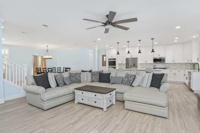 living room with sink, ceiling fan with notable chandelier, and light hardwood / wood-style flooring