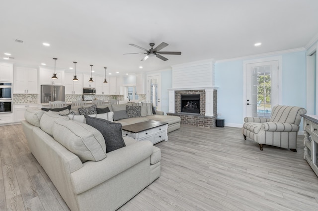 living room featuring a fireplace, ornamental molding, light hardwood / wood-style floors, and ceiling fan