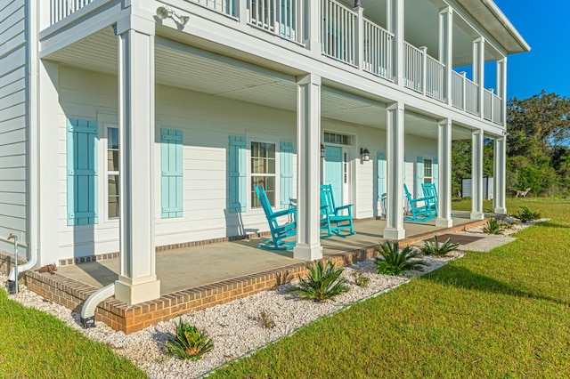 view of exterior entry featuring a balcony, a yard, and covered porch