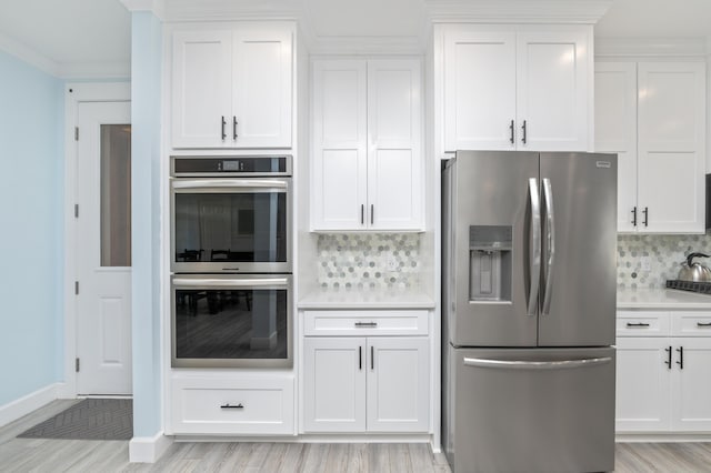 kitchen with stainless steel appliances, white cabinets, light wood-type flooring, and decorative backsplash