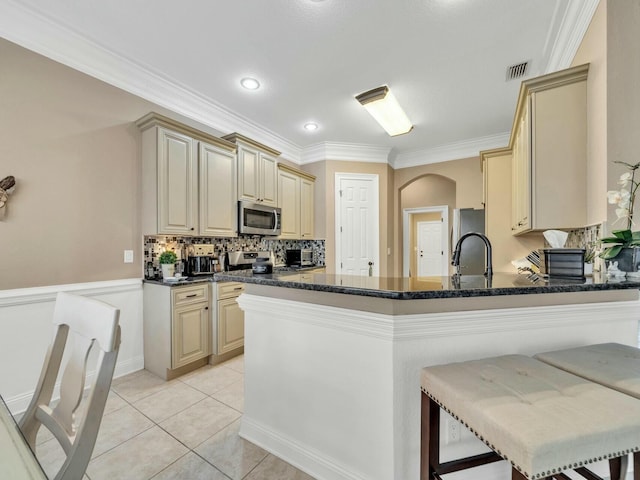 kitchen with kitchen peninsula, appliances with stainless steel finishes, ornamental molding, light tile patterned floors, and a breakfast bar area