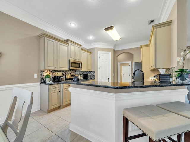 kitchen featuring kitchen peninsula, ornamental molding, stainless steel appliances, a breakfast bar area, and light tile patterned flooring