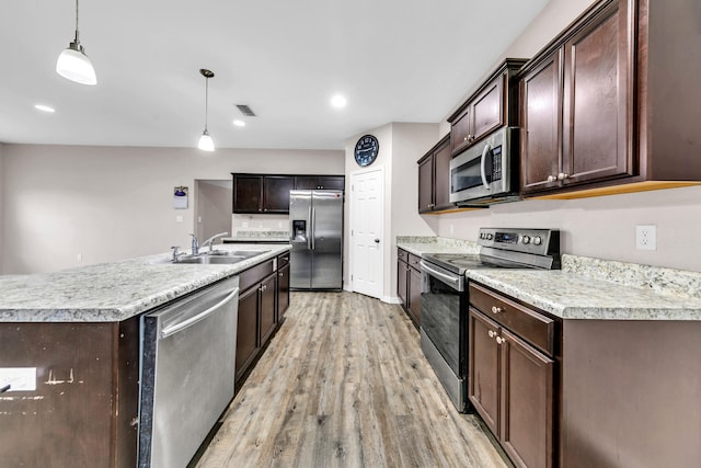 kitchen with sink, an island with sink, decorative light fixtures, appliances with stainless steel finishes, and light wood-type flooring