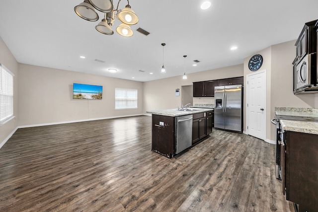 kitchen featuring decorative light fixtures, an island with sink, appliances with stainless steel finishes, and dark wood-type flooring