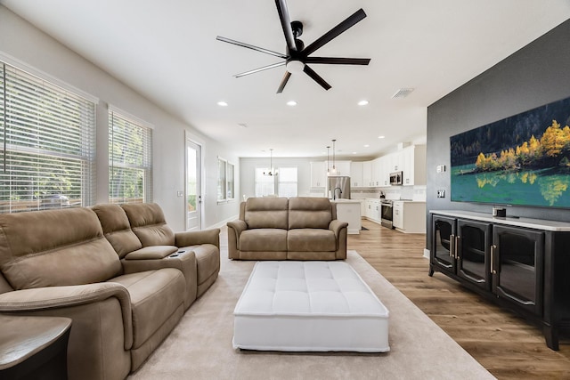 living room with ceiling fan with notable chandelier and light wood-type flooring